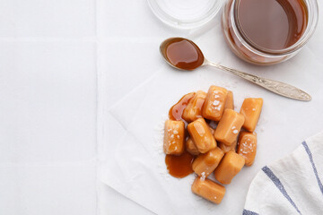 Yummy caramel candies and sea salt on white table, flat lay. Space for text