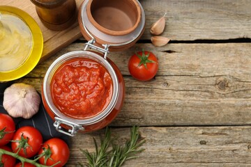 Homemade tomato sauce in jar and fresh ingredients on wooden table, flat lay. Space for text