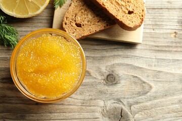 Fresh pike caviar in bowl, lemon and bread on wooden table, flat lay. Space for text
