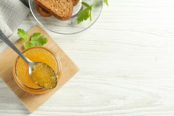 Fresh pike caviar in glass jar, parsley, bread and spoon on white wooden table, flat lay. Space for...