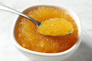 Fresh pike caviar in bowl and spoon on white table, closeup