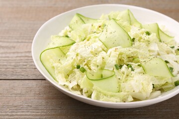 Tasty salad with Chinese cabbage, cucumber and green onion in bowl on wooden table, closeup