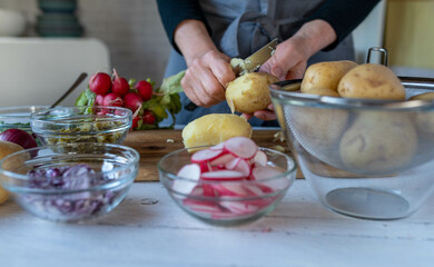 Woman peeling fresh jacket potatoes in the kitchen for making potato salad
