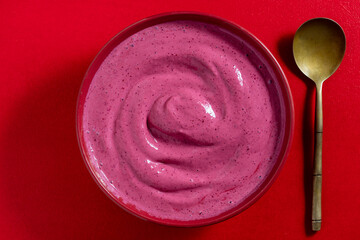 Sweet summer cherry soup in a plate on a red background, closeup, top view. Hungarian cold red cherry soup with yogurt or cream