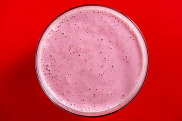 Raspberry banana smoothie in glass on a red background, closeup, top view