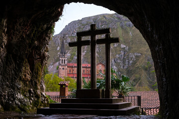 A cross is featured prominently in a cave, with a mountain looming in the background. The rugged...