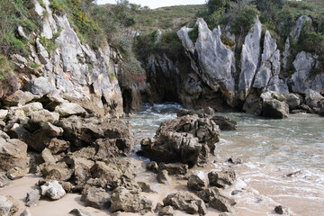 A rocky beach in Llanes, Asturias, featuring a body of water enclosed by large rocks. The beach is...