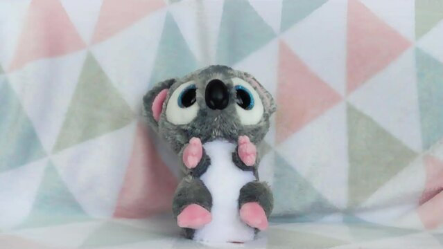 Stuffed and fluffy plush toy koala falls onto a soft baby blanket. Slow motion.
