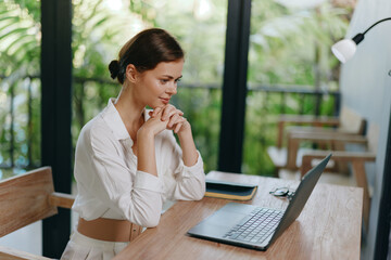 Smiling Freelancer Working on Laptop at Home Office A cheerful young woman with a laptop sits at...