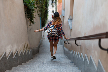 beautiful tourist girl in fashionable clothes with a backpack goes down and jumps down the stairs. Woman traveling in the city