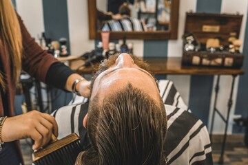 Man enjoys luxurious haircare at upscale barber shop. Female barber provides top-notch service, ensuring client relaxation and hair health.