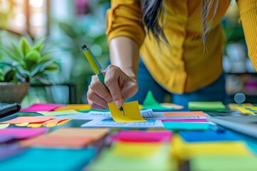 Naklejka premium Focused person placing sticky notes on paper, hands only visible, surrounded by vibrant color-coded office stationery, concept of organization.