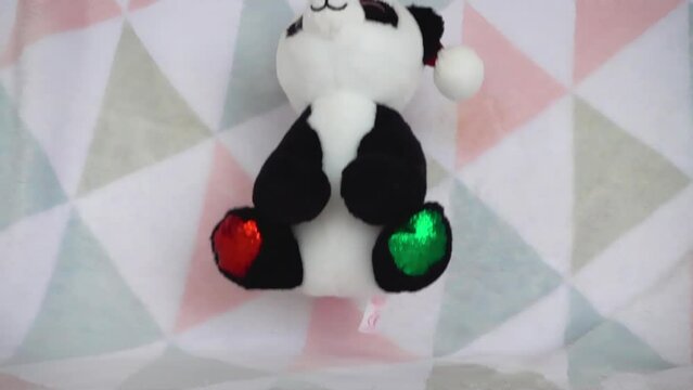 Stuffed and fluffy teddy toy panda bear in a Santa Claus hat fall on a soft baby blanket. Slow motion.