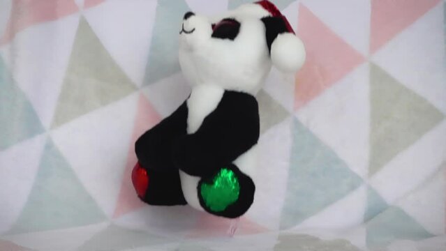 Stuffed and fluffy teddy toy panda bear in a Santa Claus hat fall on a soft baby blanket. Slow motion.