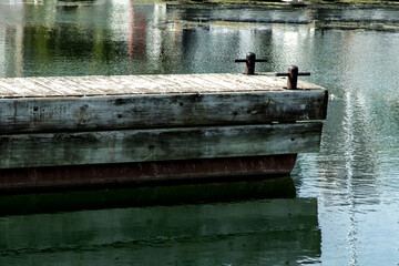 A marina floating dock with two mooring cleats in still water with reflections of boats