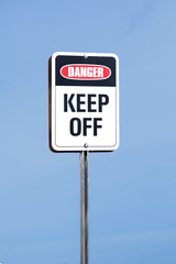 Danger KEEP OFF sign red black and  white on a clear blue sky