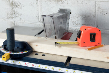 A table saw in a workshop with a piece of pine wood and a tape measure and a pencil ready to mark...