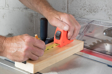 a carpenter in a workshop marks a piece of pine wood with a tape measure and a pencil lying on a...