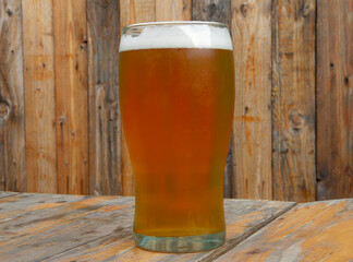 Closeup view of a full glass of honey golden beer with a rustic wooden background	
