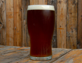 Craft beer. Closeup view of a red ale with perfect foam in a glass on the white marble table with a wooden background.	