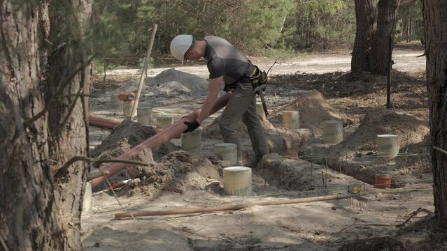 Construction Worker Laying Underground Pipes in a Forested Area During Daylight