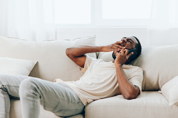 Happy African American man sitting on a black sofa at home, confidently typing a message on his mobile phone while enjoying a video call with a friend The modern apartment provides a comfortable