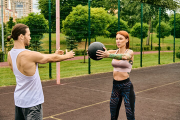 A man and woman in sportswear playfully exercise with a ball outdoors, showcasing determination and...