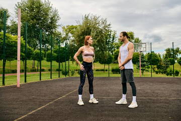 A man and woman, wearing sportswear, stand on a basketball court, showcasing determination and...