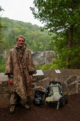 A man in a camo rain poncho smiles at the camera in front of Eugina waterfall on the Bruce Trail, Niagara Escarpment
