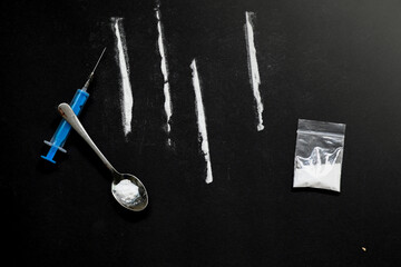 cocaine lines with a syringe and a spoon, a bag full of heroin on a black background. stop drugs