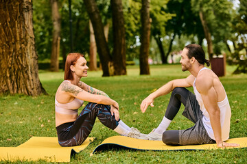 A in sportswear sit on a mat in the park, led by a personal trainer, displaying determination and...