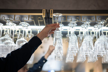 Bartender Reaching for a Clean Glass From a Hanging Rack Above the Bar Counter
