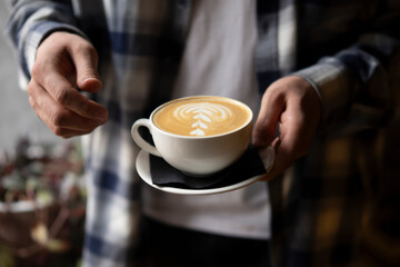 Person's hands Holding a Freshly Made Cappuccino With Artful Foam Design