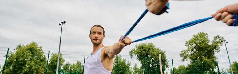 A man wearing sportswear, holding a blue resistance band outdoors.