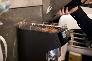 Pouring Fresh Coffee Beans Into an Electric Grinder at a Modern Cafe