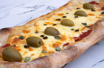 Closeup view of a mozzarella cheese pizza with olives and fresh oregano leaves, on the white marble...