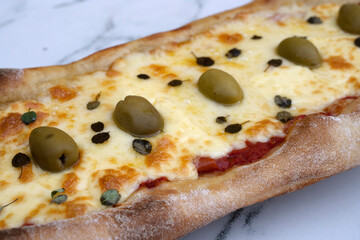 Closeup view of a mozzarella cheese pizza with olives and fresh oregano leaves, on the white marble table.
