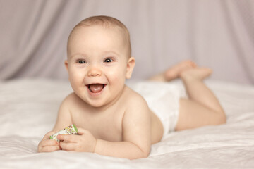 Portrait of cute  naked Caucasian baby crawling on bed on the white blanket in bedroom. Smiling  kid lying on tummy