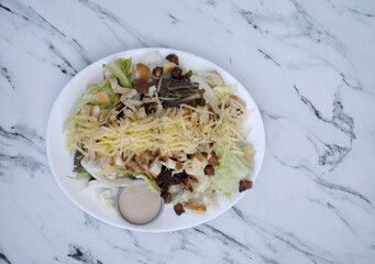 Caesar salad. Top view of fresh a salad with lettuce, parmesan cheese, bread croutons, sliced grilled chicken breast, bacon and Caesar dressing on the white marble table.	
