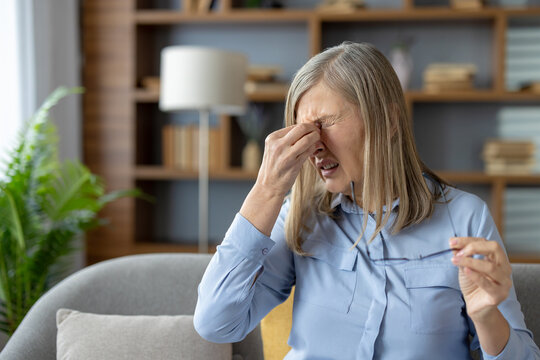 Mature woman at home touching her temples, feeling overwhelmed and stressed. She appears distressed and in need of comfort.