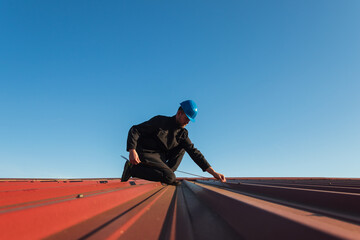 Young man worker in helmet holding meter tape on roof with blue sky. Roofer work background