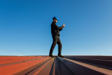 Young man worker in helmet standing on roof using mobile phone with blue sky. Roofer work background - 783249304