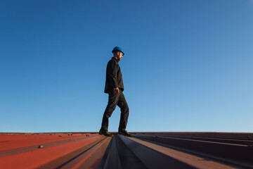 Young man worker in helmet standing on roof with blue sky. Roofer work background - 783249305