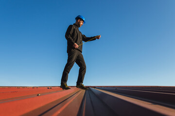 Young man worker in helmet holding meter tape on roof with blue sky. Roofer work background - 783249316