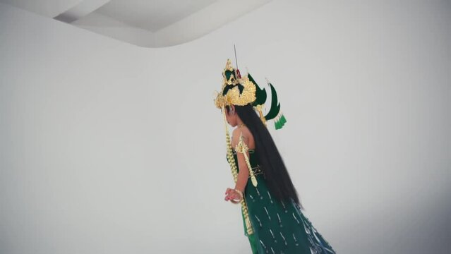 Traditional Asian performer in elaborate costume and headdress against a plain background, side view.