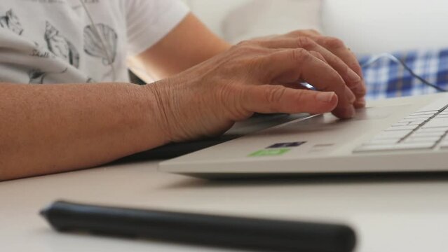 Dettaglio ravvicinato delle mani di una persona anziana o adulta mentre digita sulla tastiera di un computer laptop bianco, con penna digitale sfocata in primo piano