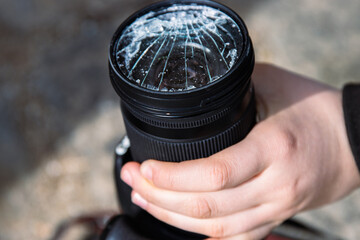 Hands of young photographer holding DSLR photo camera with  broken lens filter glass after if fall...