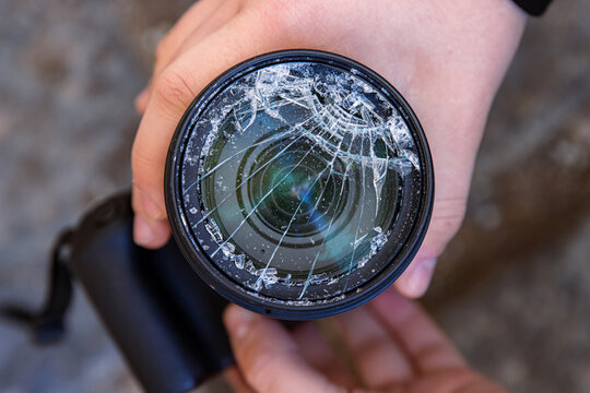 Hands of young photographer holding DSLR photo camera with  broken lens filter glass after if fall down onto the floor. Close up. Destroyed cracked photo-filter. Macro. Top view. Selective focus.