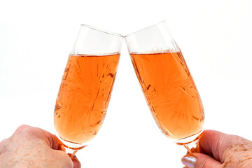 Two people raising a celebratory toast with two cut glass crystal flute glasses of pink champagne.