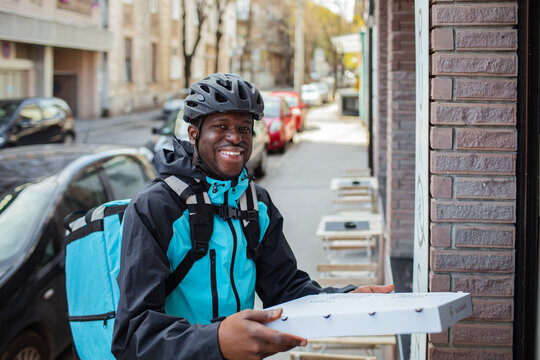 Happy delivery man with a pizza box on a city street